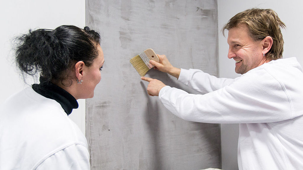 Malermeister und Auszubildende beim Verputzen einer Wand